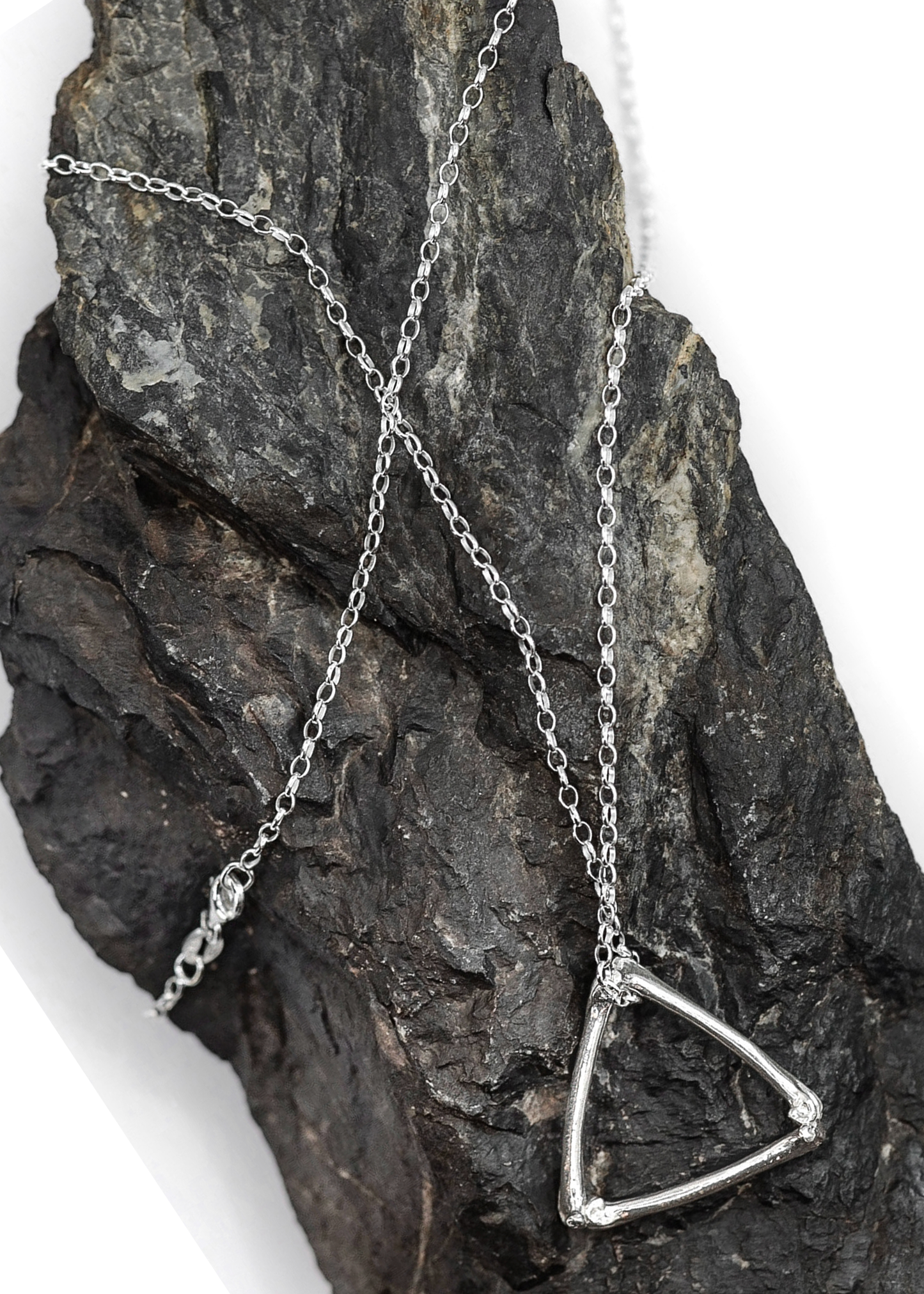 Silver necklace with a triangle pendant on a textured stone surface