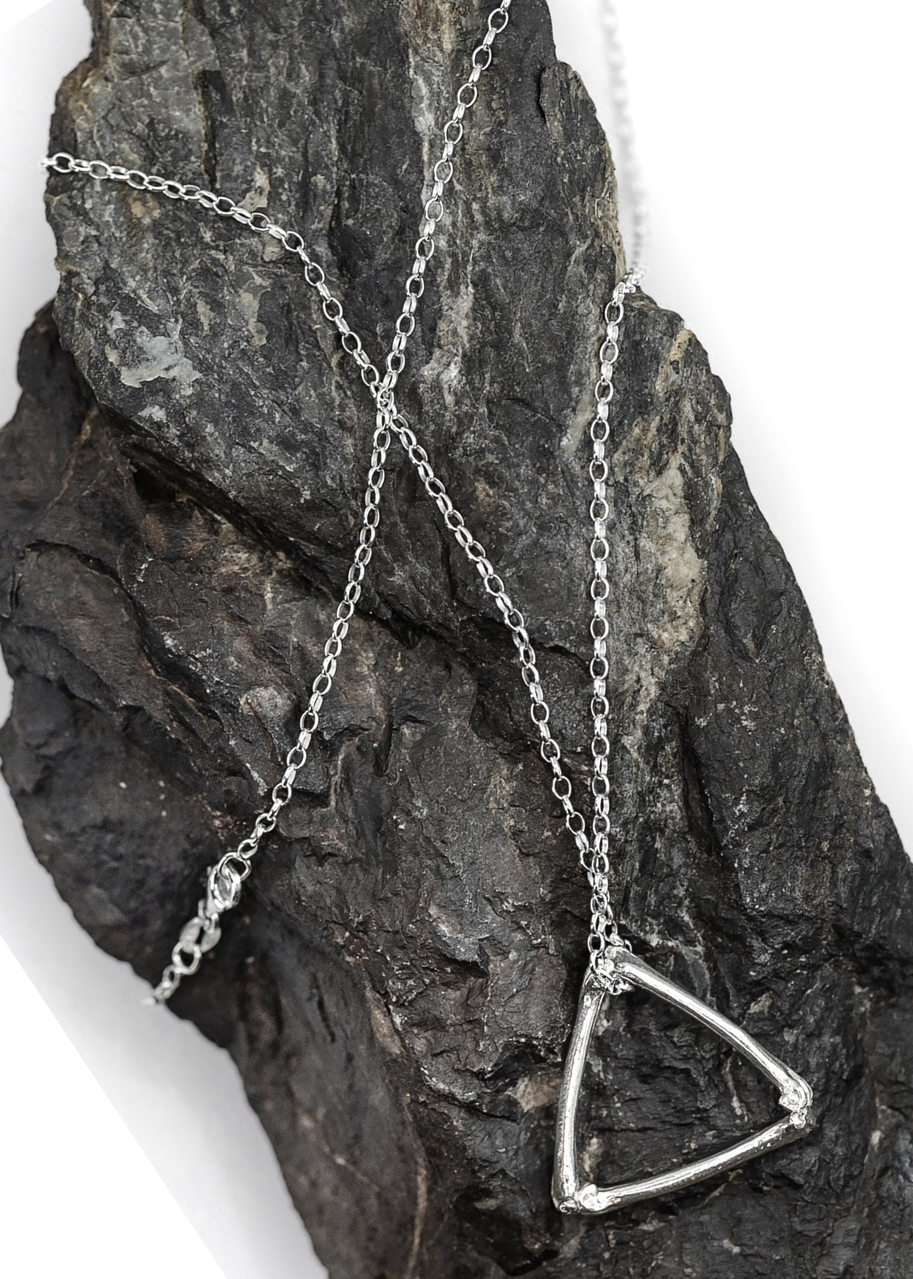 Silver necklace with a triangle pendant on a textured stone surface