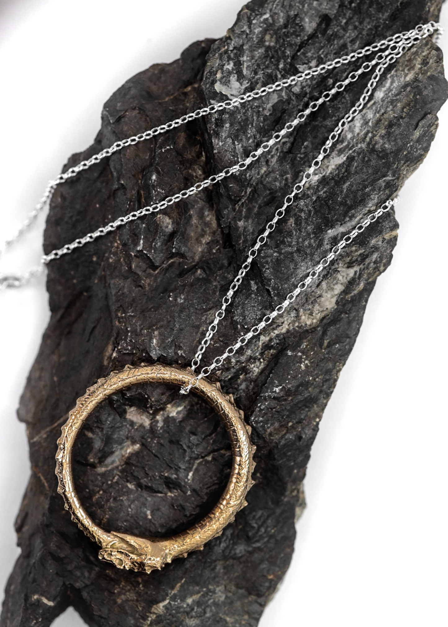 Necklace with a circular ouroboros serpent design pendant on a dark stone surface