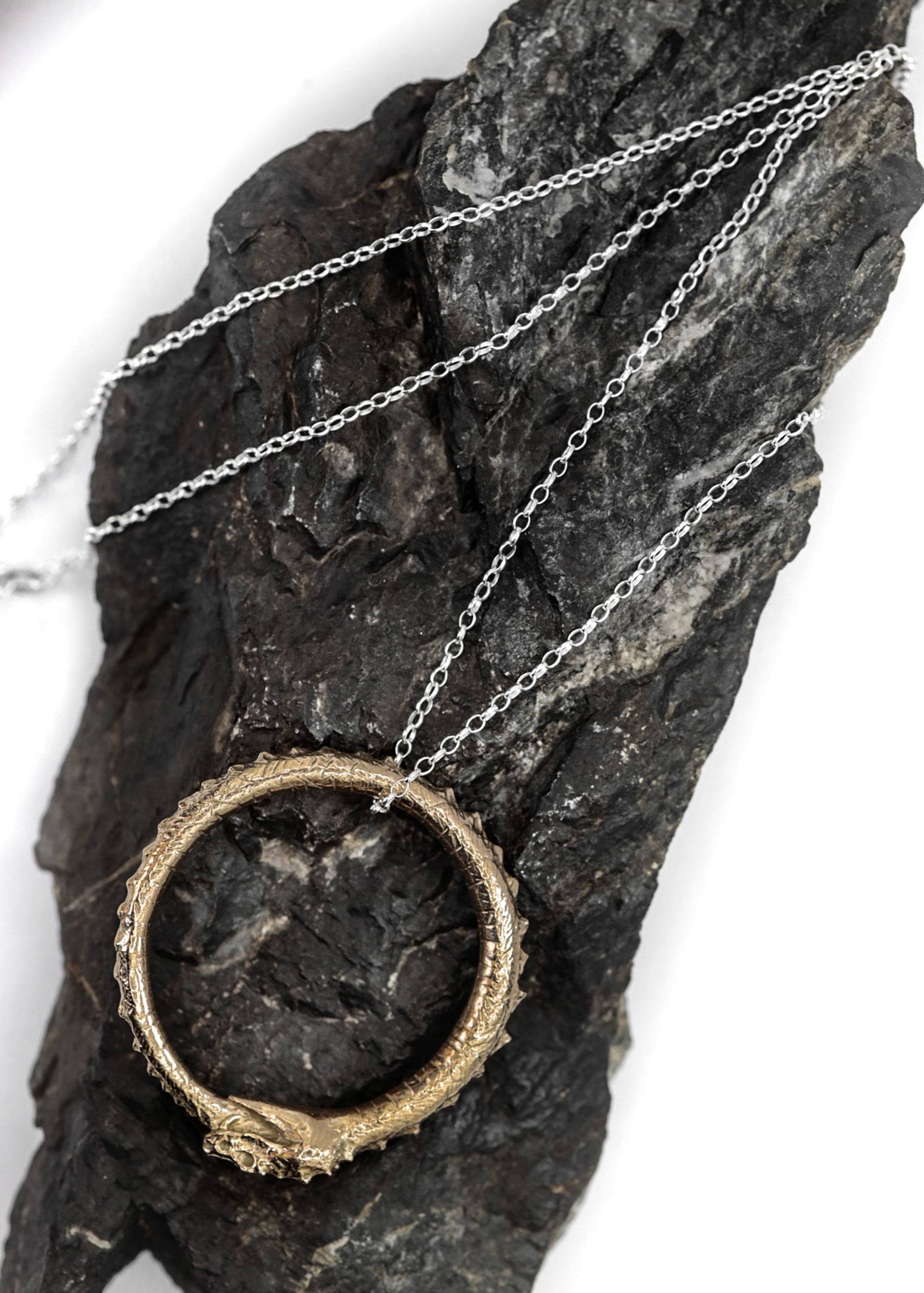 Necklace with a circular ouroboros serpent design pendant on a dark stone surface